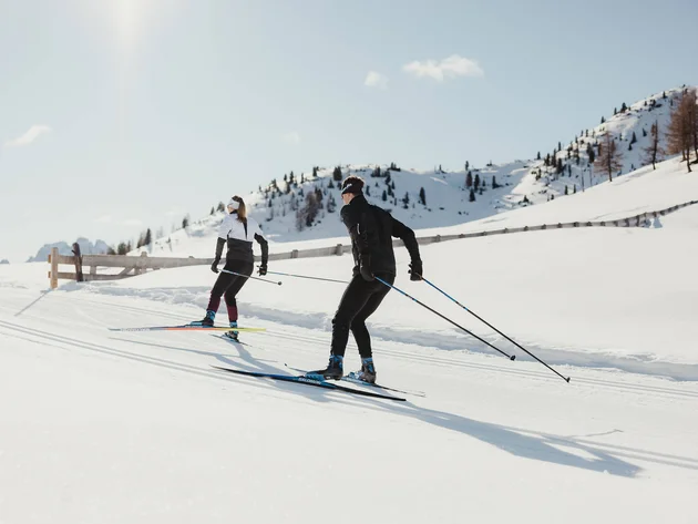 Two cross-country skiers on snowy mountains under bright sunlight