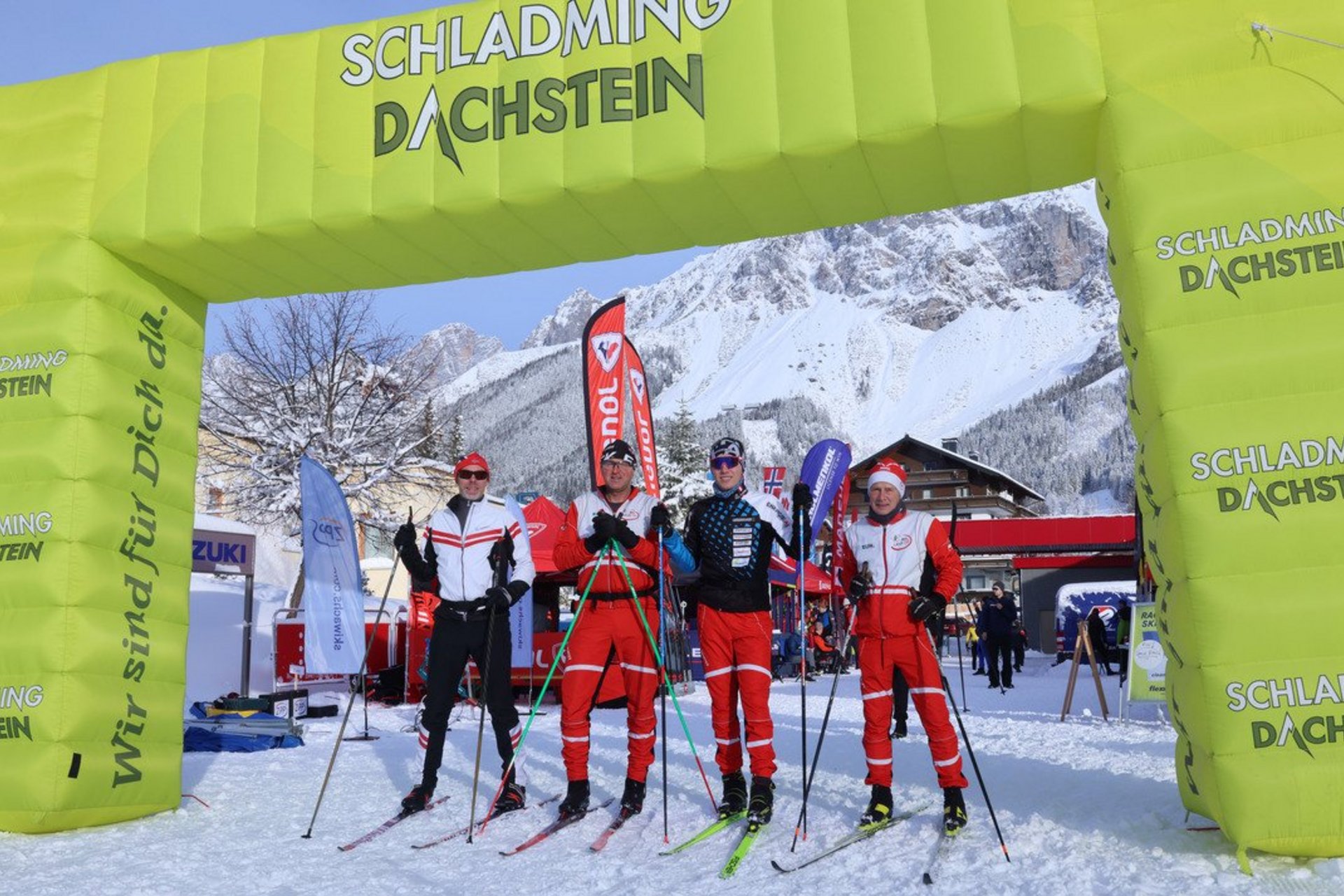 Cross Country Ski Holidays © Hans Simonlehner Four skiers stand under a yellow Schladming Dachstein arch in the snow