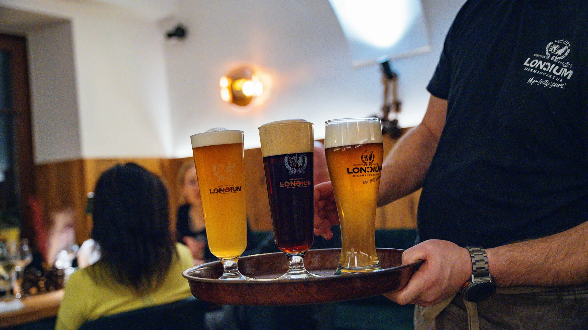 Kellner trägt Tablett mit drei verschiedenen Bieren in einem Restaurant