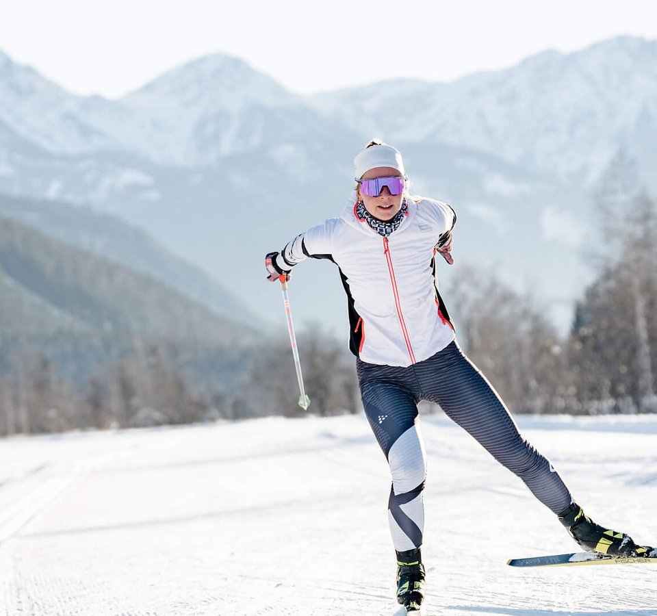 Langläuferin in weißer Jacke auf verschneiter Loipe vor Bergen