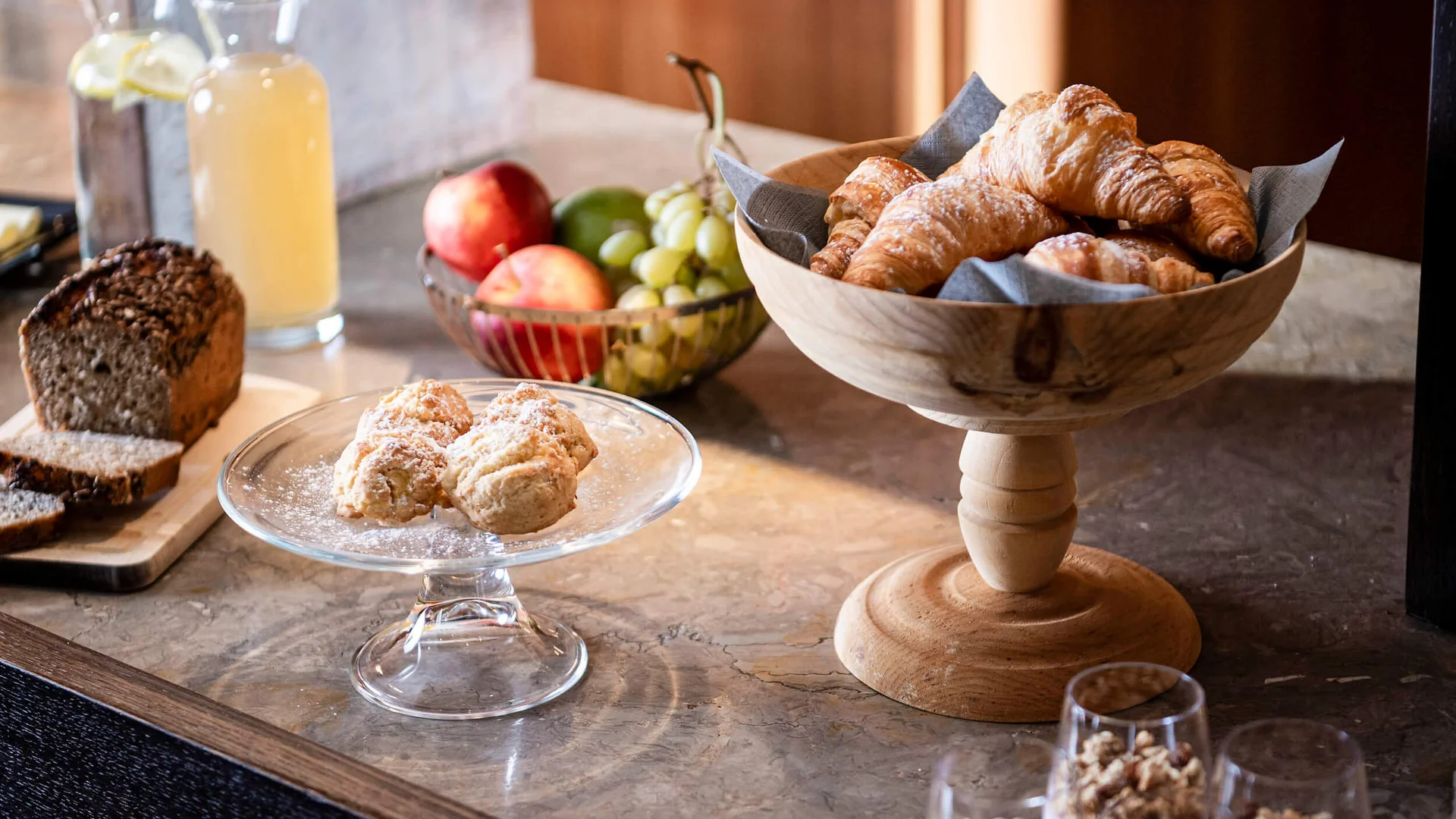 Frühstück mit Croissants, Brötchen, Obst und Getränken auf dem Tisch