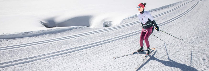 Woman cross-country skiing on a sunny, snow-covered trail