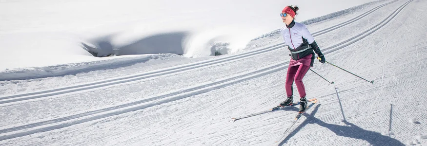 Woman cross-country skiing on a sunny, snow-covered trail