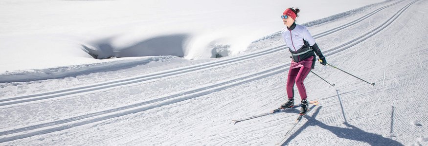 Frau beim Langlaufen auf einer sonnigen, schneebedeckten Loipe