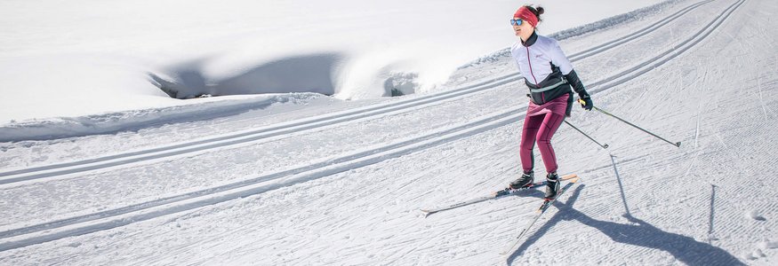 Frau beim Langlaufen auf einer sonnigen, schneebedeckten Loipe