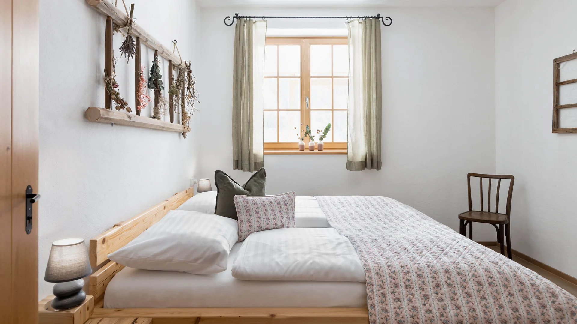 SLOHO Bergurlaub Apartments © Cathrine Stukhard Helles Schlafzimmer mit Holzbett, Fenster, Sessel und dekorativem Wandregal