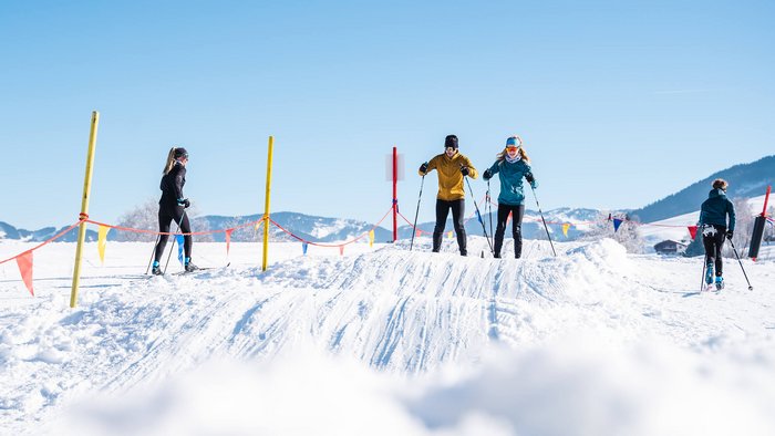 Vier Menschen beim Langlaufen auf verschneiter Strecke bei klarem Himmel