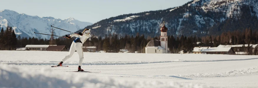 Langläufer in weißer Kleidung auf verschneiter Berglandschaft mit Kirche