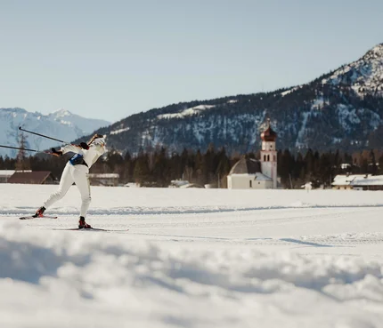 Region Seefeld - Tirols Hochplateau © Alex Moling Langläufer in weißer Kleidung auf verschneiter Berglandschaft mit Kirche