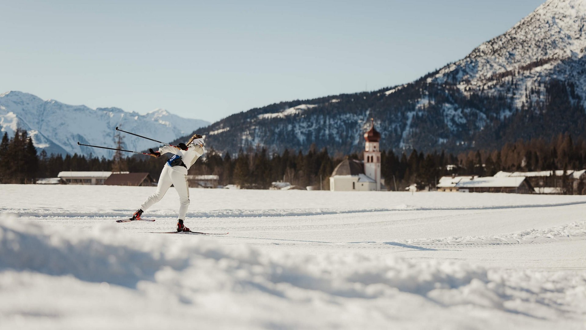Langläufer in weißer Kleidung auf verschneiter Berglandschaft mit Kirche