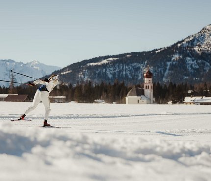 Langläufer in weißer Kleidung auf verschneiter Berglandschaft mit Kirche