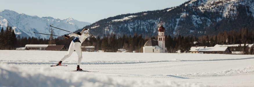 Langläufer in weißer Kleidung auf verschneiter Berglandschaft mit Kirche