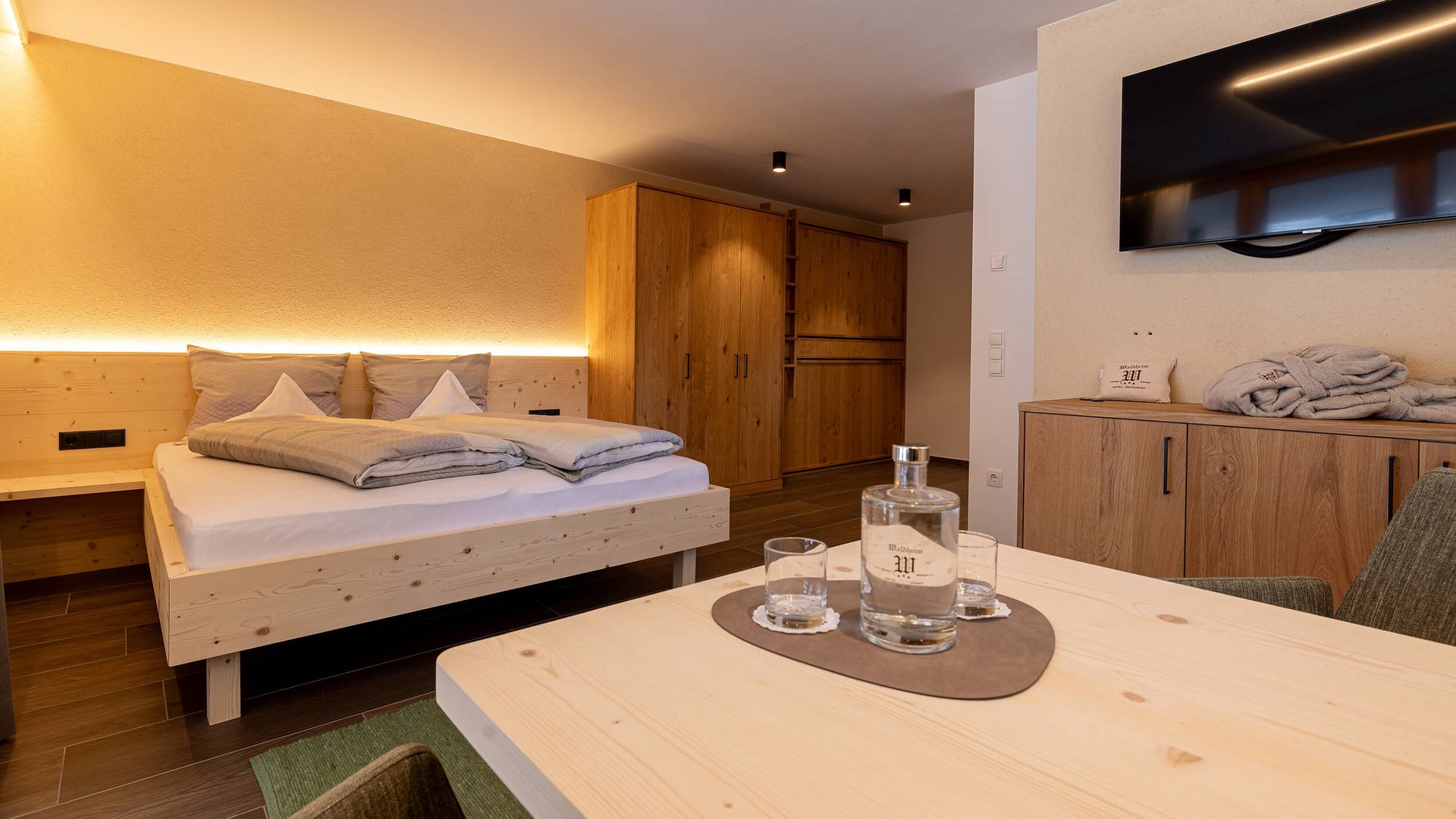 Gemütliches Hotelzimmer mit Holzbetten, Schrank und Tisch mit Wasserflasche und Gläsern.