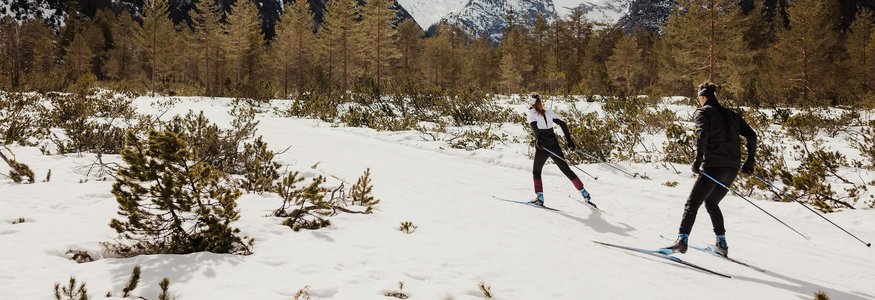 Zwei Langläufer im verschneiten Gebirgstal vor schneebedeckten Bergen
