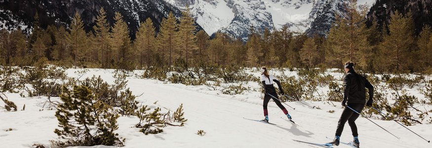 Zwei Langläufer im verschneiten Gebirgstal vor schneebedeckten Bergen