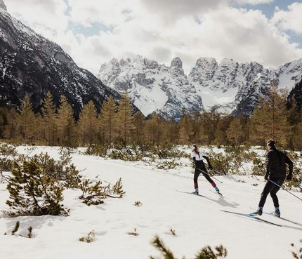 Two cross-country skiers in a snowy mountain valley with snow-covered peaks