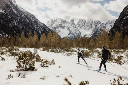 Zwei Langläufer im verschneiten Gebirgstal vor schneebedeckten Bergen
