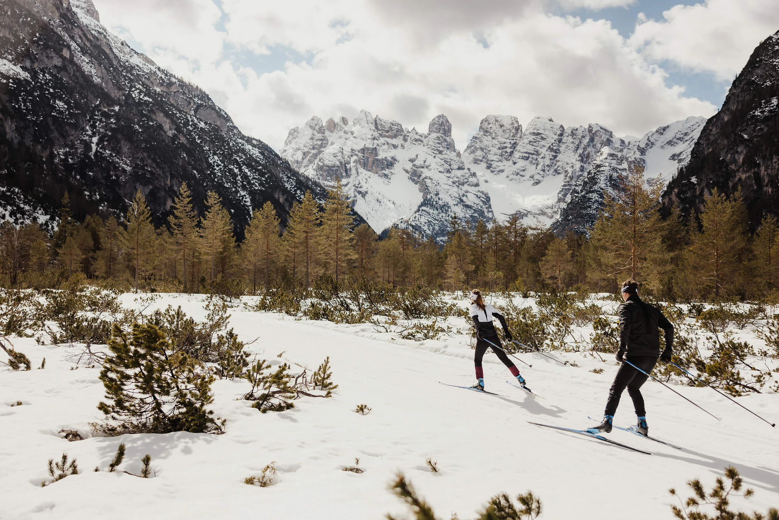 Zwei Langläufer im verschneiten Gebirgstal vor schneebedeckten Bergen