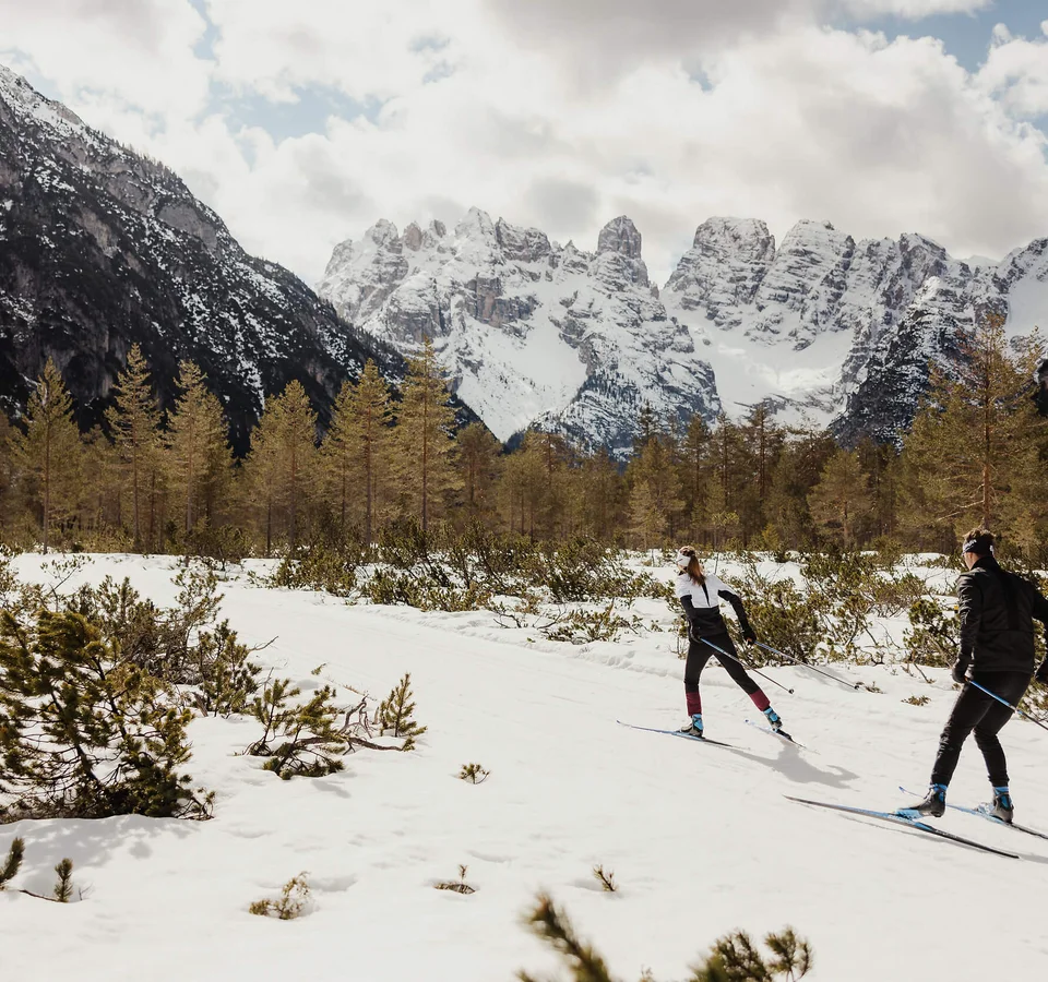 Zwei Langläufer im verschneiten Gebirgstal vor schneebedeckten Bergen