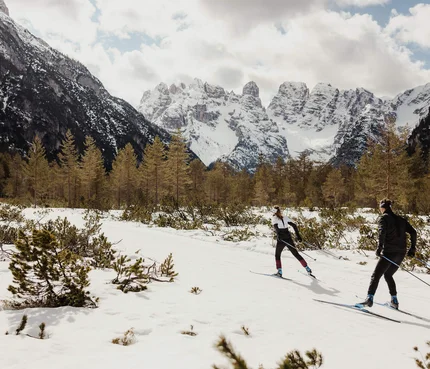 Zwei Langläufer im verschneiten Gebirgstal vor schneebedeckten Bergen