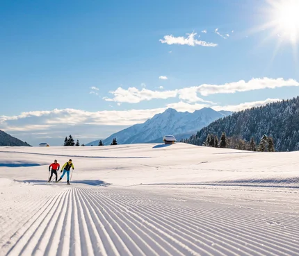 Two cross-country skiers on groomed snow trail in sunny mountain landscape