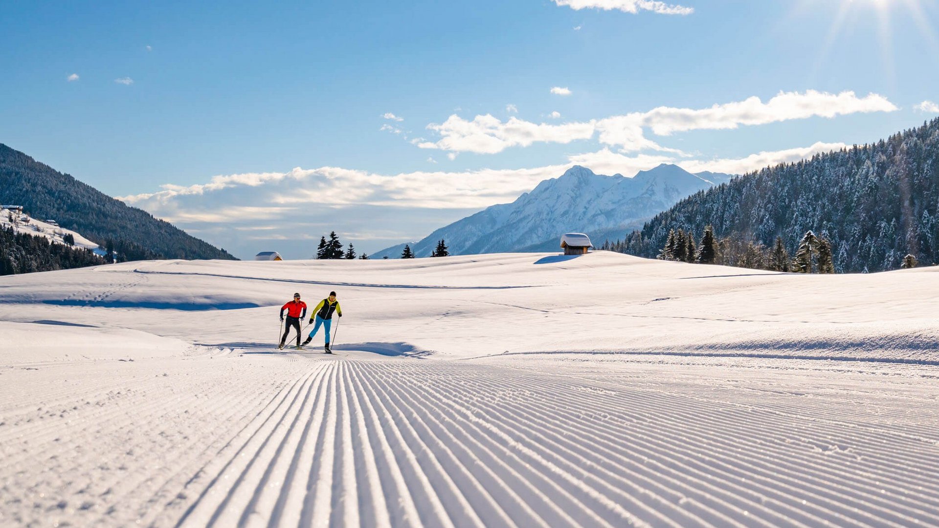 Zwei Langläufer auf präparierter Schneeloipe in sonniger Berglandschaft