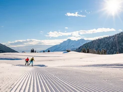 Two cross-country skiers on groomed snow trail in sunny mountain landscape
