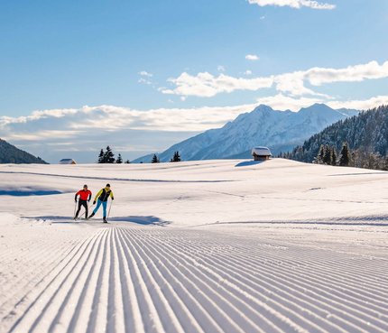 Zwei Langläufer auf präparierter Schneeloipe in sonniger Berglandschaft