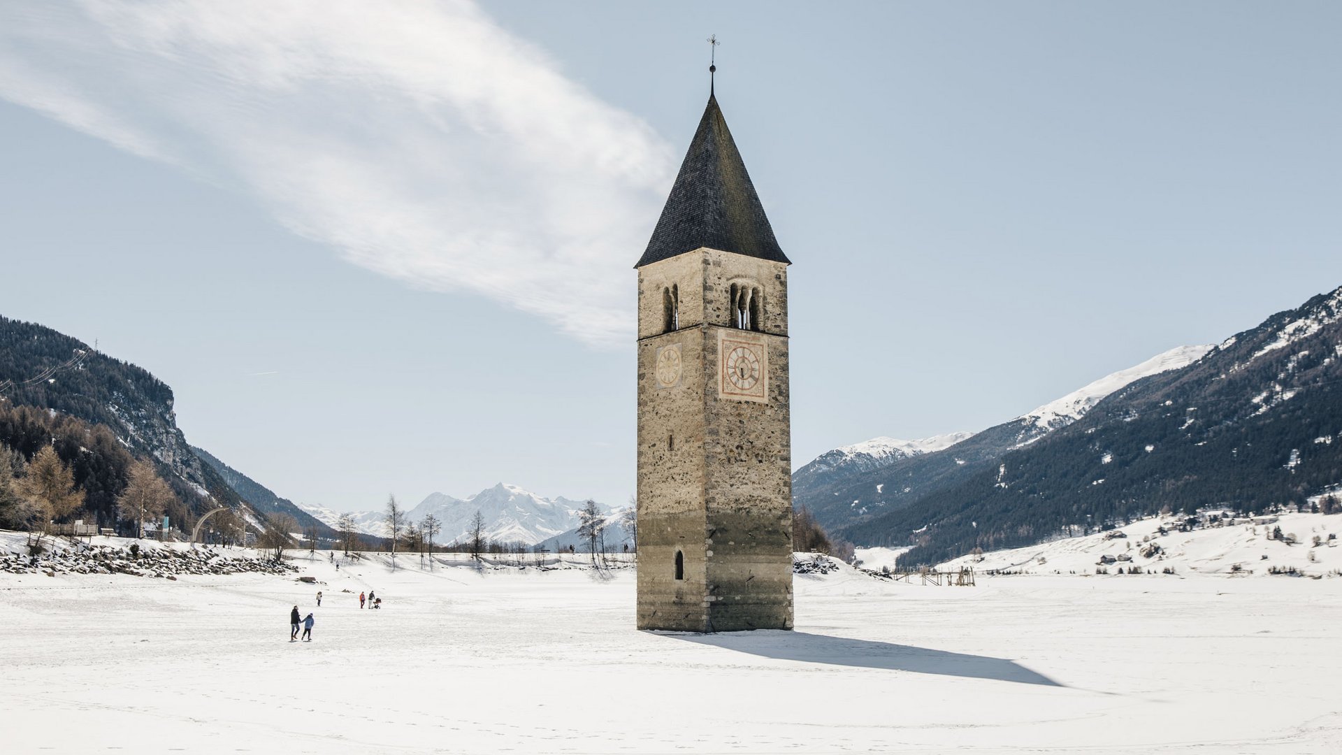 Kirchturm ragt aus zugefrorenem See mit schneebedeckten Bergen im Hintergrund
