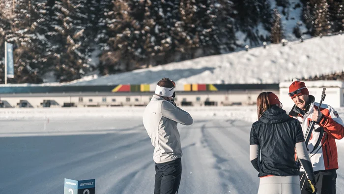 Biathlet beim Schießtraining auf verschneiter Bahn mit Trainern.