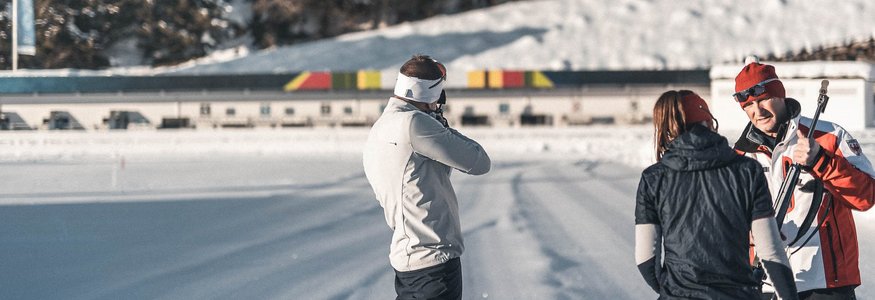 Biathlet beim Schießtraining auf verschneiter Bahn mit Trainern.