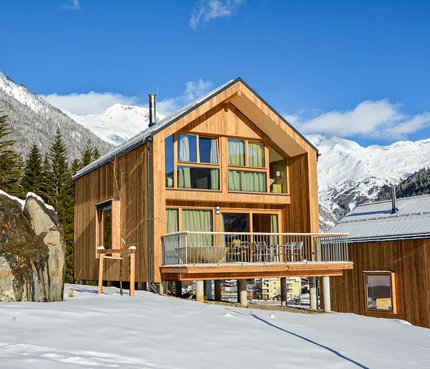 Modernes Holzhaus in verschneiter Berglandschaft unter blauem Himmel