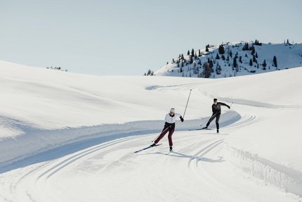 Zwei Personen beim Langlaufen auf verschneiter Bergstrecke unter klarem Himmel