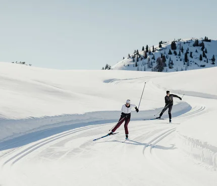 Zwei Personen beim Langlaufen auf verschneiter Bergstrecke unter klarem Himmel