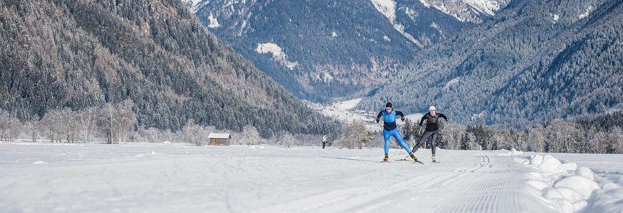 Skilangläufer auf verschneiter Strecke vor Bergkulisse in winterlicher Landschaft