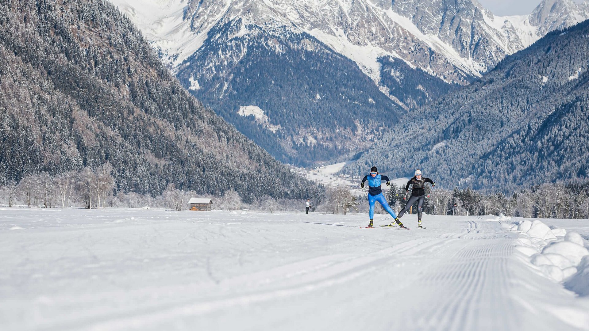 Skilangläufer auf verschneiter Strecke vor Bergkulisse in winterlicher Landschaft