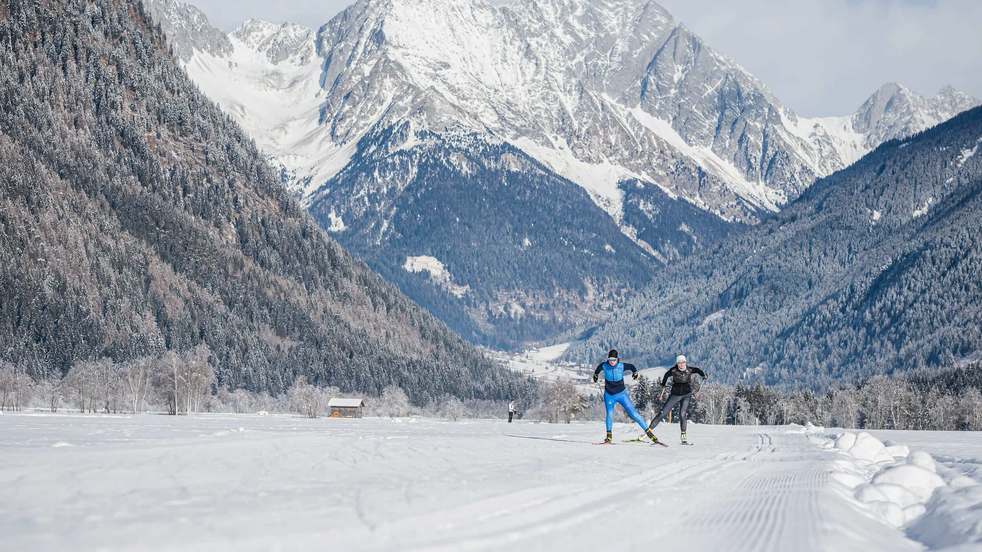 Trails & trail reports © Harald Wisthaler Cross-country skiers on snowy trail with mountain backdrop in winter scenery