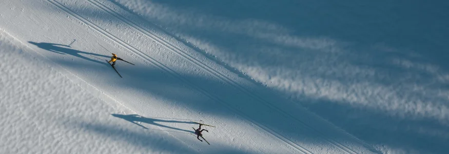 Zwei Langläufer auf schneebedeckter Spur mit langen Schatten im Morgenlicht