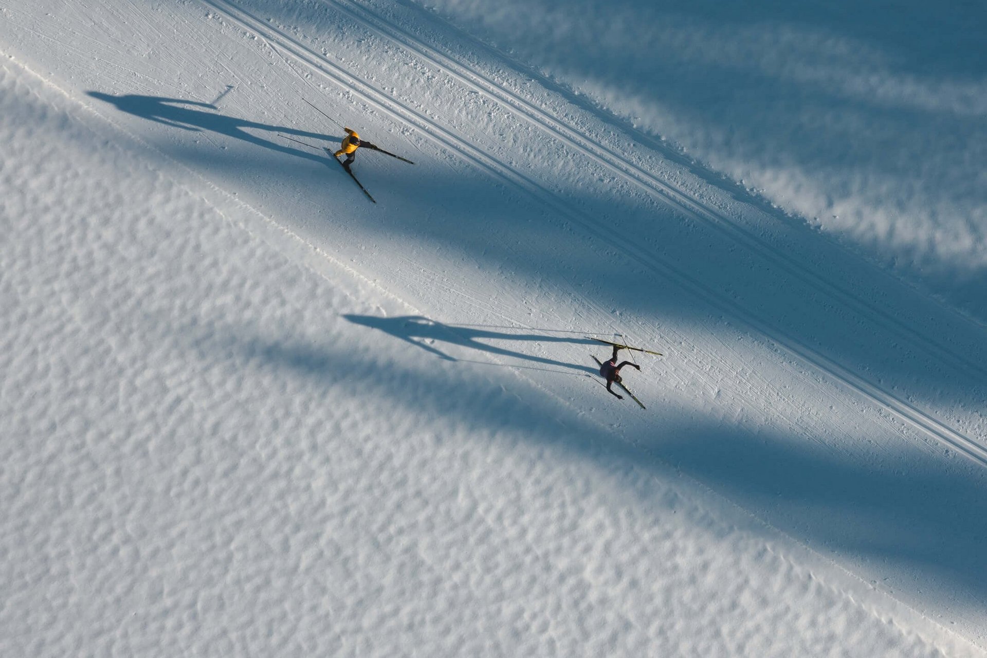 Zwei Langläufer auf schneebedeckter Spur mit langen Schatten im Morgenlicht