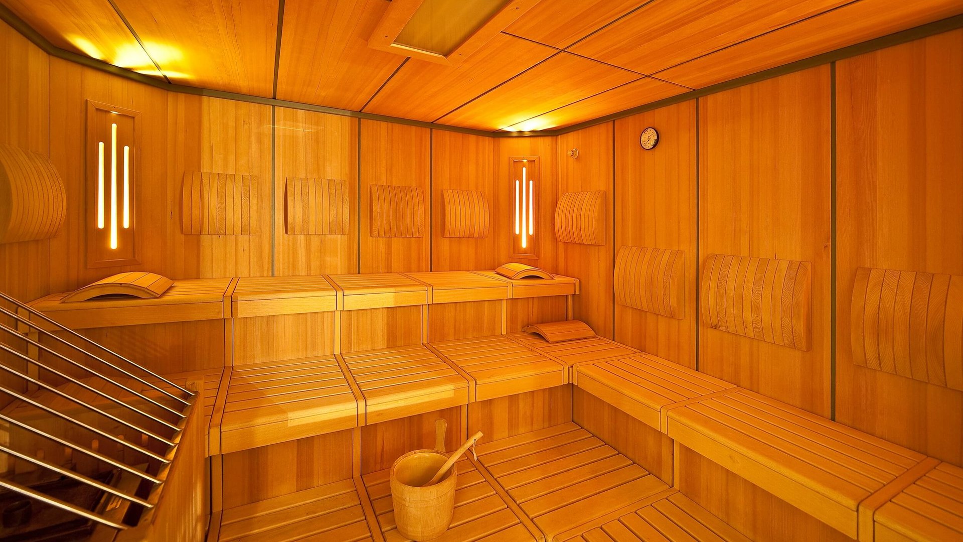 Innenraum einer hell beleuchteten Holzsauna mit Sitzbänken und Holzeimer
