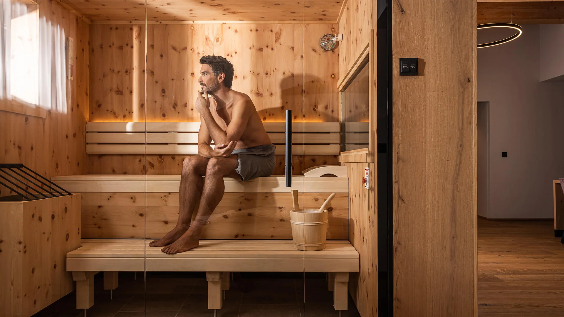 Mann entspannt in einer Sauna aus Holz, sitzt nachdenklich auf der Bank