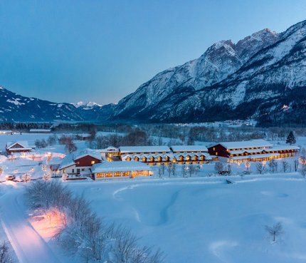 Dolomitengolf Hotel & Spa © Martin Lugger Verschneite Häuser im Tal vor beleuchteten Bergen bei Dämmerung