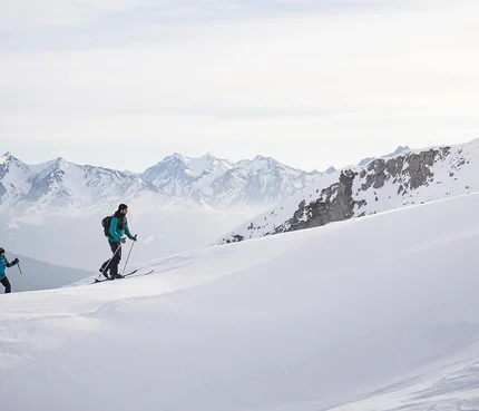 Zwei Skifahrer steigen einen schneebedeckten Berg mit Bergen im Hintergrund hinauf