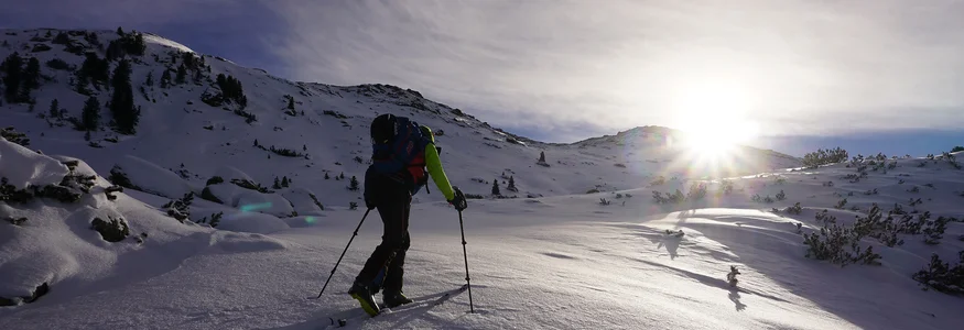 Skier climbing snowy mountain with sun setting in the background