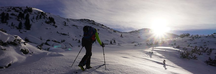 Skifahrer steigt bei Sonnenuntergang auf verschneitem Berg auf