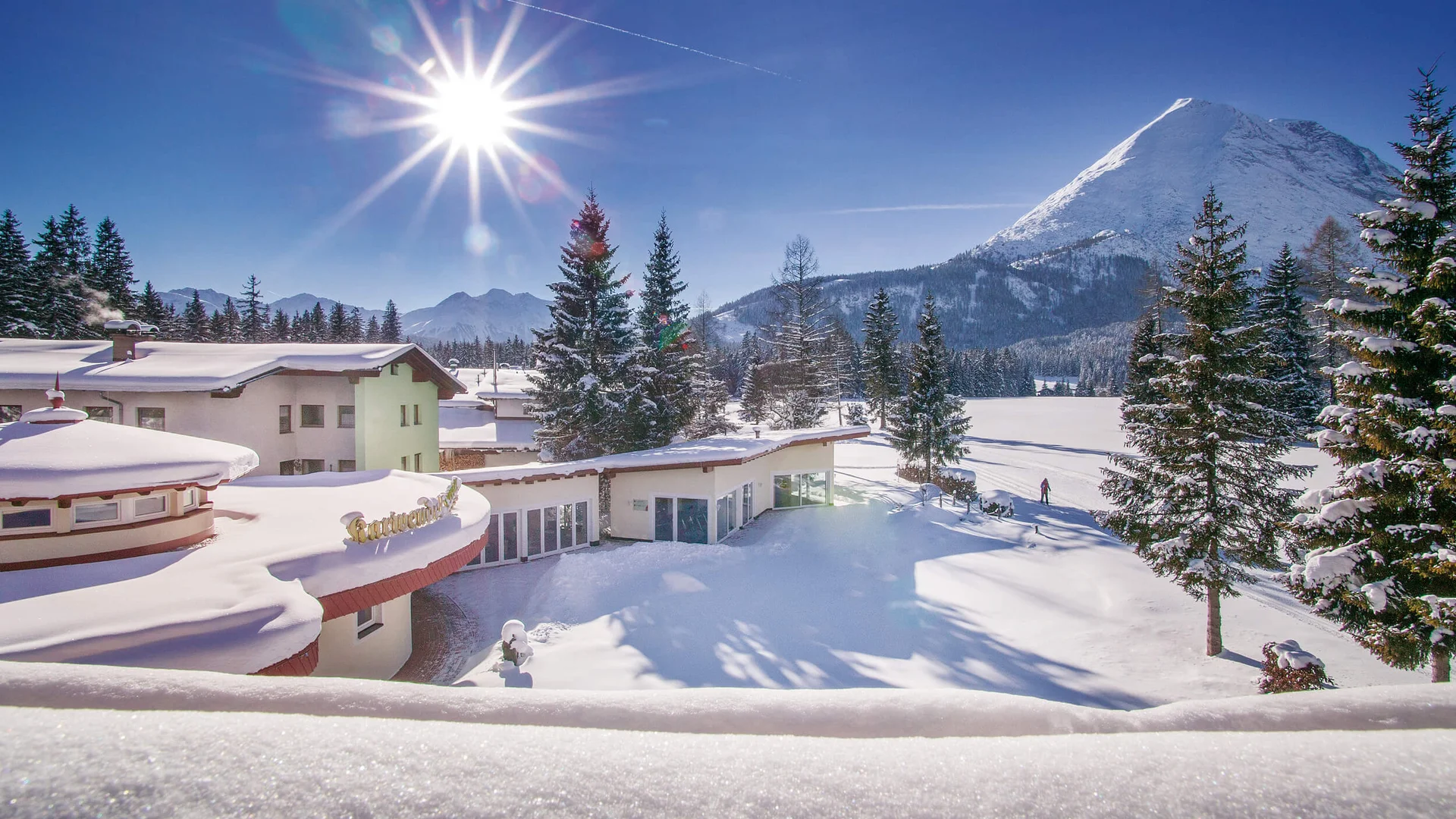 Alpenhotel Karwendel **** © Hotel Karwendel Bernhard Rödlach BetriebsGmbH Schneebedeckte Häuser und Bäume vor sonnigem Bergpanorama