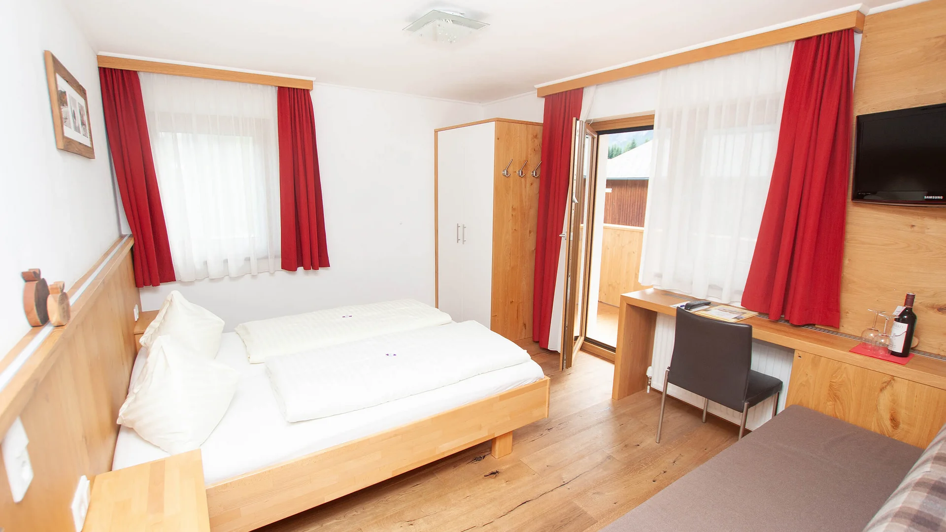 Helles Hotelzimmer mit Bett, Schreibtisch, Fernseher und Balkon