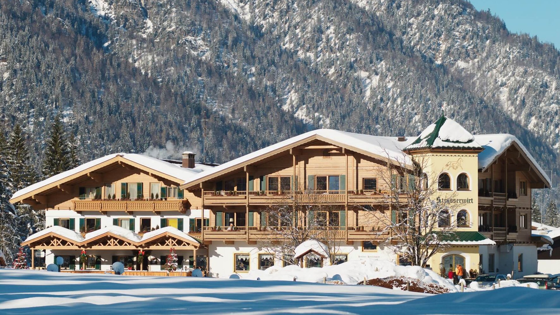 Snow-covered old wooden house in front of forested mountain in winter