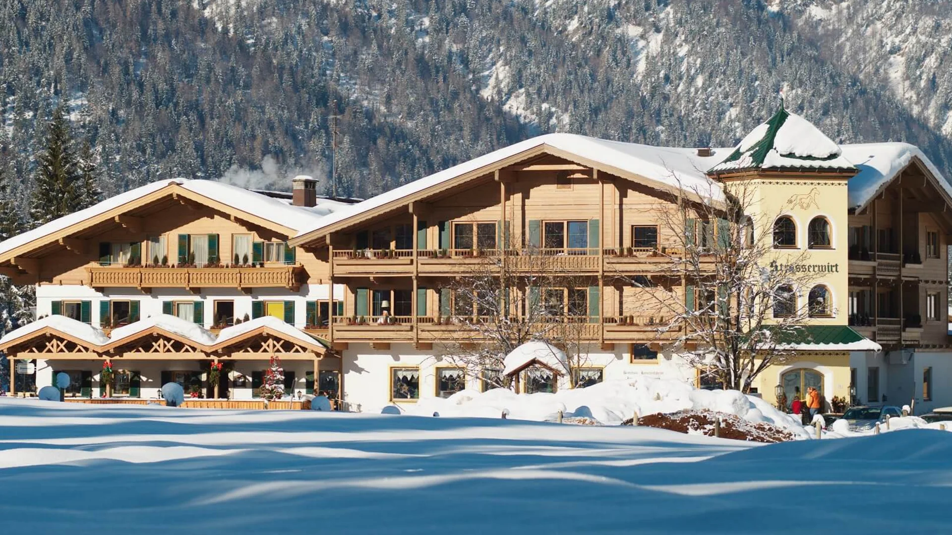Snow-covered old wooden house in front of forested mountain in winter