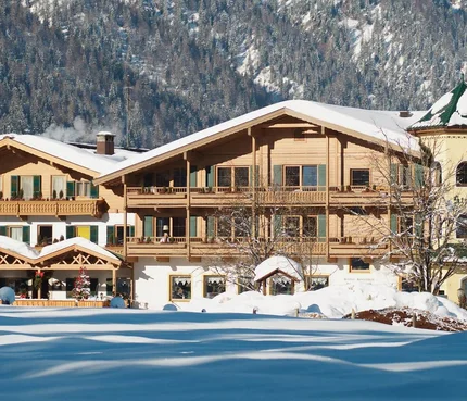 Snow-covered old wooden house in front of forested mountain in winter